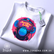 Футболка Another Life білого кольору, складена на поверхні, ракурс зверху, фон світло-сірий, принт з малюнком мавпи в окулярах віртуальної реальності, яскраві кольори принта: рожевий, синій, жовтий, на етикетці зелена стрічка.