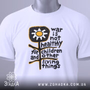 Футболка антивоєнна позиція, біла, складена на столі, фон світло-сірий, принт з жовтою квіткою та текстом чорного кольору, з етикеткою зеленого кольору.