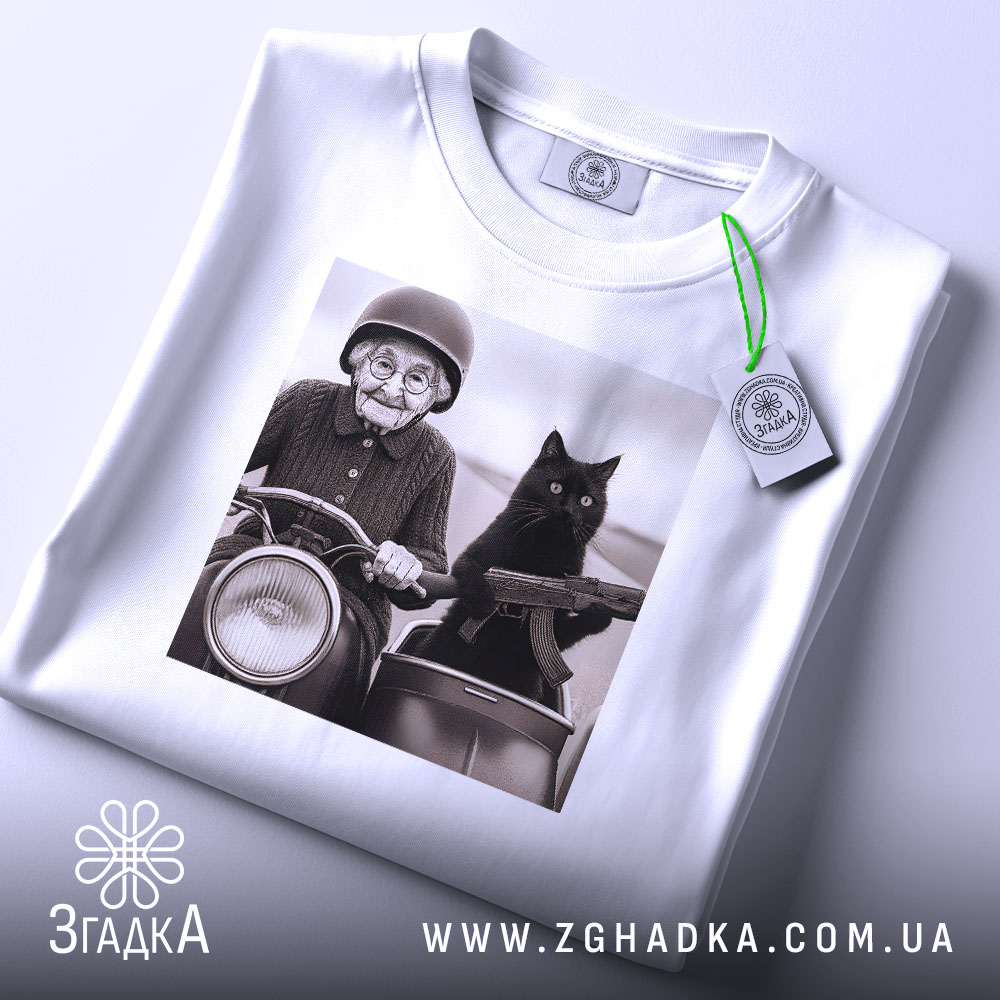 Футболка бабуся і автомат. Біла футболка, на якій зображена бабуся з котом на мотоциклі, з етикеткою, що звисає. Ракурс зверху, фон світлий. Принт яскравий, з акцентом на обличчя бабусі та кота.