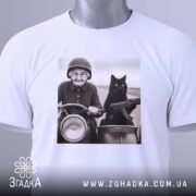 Футболка бабуся і автомат. Біла футболка, на якій зображена бабуся з котом на мотоциклі, з етикеткою, що звисає. Ракурс зверху, фон світлий. Принт яскравий, з акцентом на обличчя бабусі та кота.