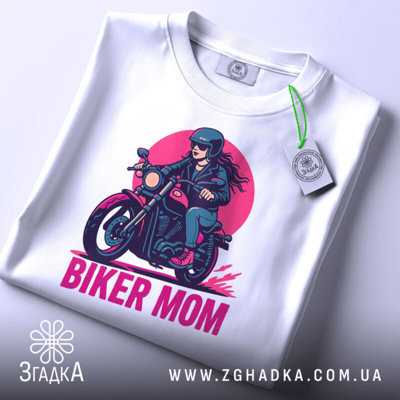 Футболка байкер мама сила. Біла футболка, складена на поверхні, з принтом жінки на мотоциклі, ракурс зверху, фон світло-сірий, принт яскравий з червоним і чорним кольорами.