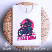 Футболка байкер мама сила. Біла футболка, складена на плетеній основі, з принтом жінки на мотоциклі, ракурс зверху, фон світло-сірий, принт яскравий з червоним і чорним кольорами.
