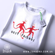 Футболка бесті друзі демони, біла, складена на столі, фон світло-сірий, принт з двома червоними демонами, які тримаються за руки, текст 'BEST FRIENDS' під ними, на футболці є етикетка.