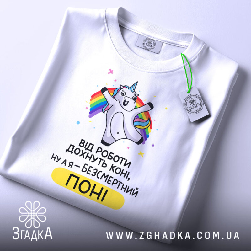 Футболка безсмертний поні, білого кольору, розкладена на поверхні, фон світло-сірий, принт з поні, що радісно піднімає руки, текст чорного кольору з жовтим акцентом, на комірці видна етикетка.