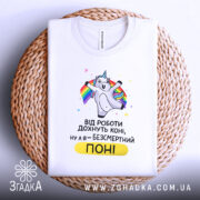 Футболка безсмертний поні, білого кольору, складена на плетеній кошику, фон світло-сірий, принт з поні, що радісно піднімає руки, текст чорного кольору з жовтим акцентом, видно етикетку на комірці.