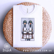 Футболка бойові гуси, біла, зображена зверху на плетеному кошику, фон світло-сірий, принт з двома гусами в військових шоломах і з автоматами, на футболці видно етикетку.