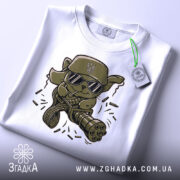 Футболка бойовий кіт, біла, зображена на столі, фон світло-сірий, принт з кумедним котом у військовій кепці та окулярах, прикріплена етикетка з логотипом.