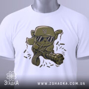 Футболка бойовий кіт, біла, зображена на столі, фон світло-сірий, принт з кумедним котом у військовій кепці та окулярах, прикріплена етикетка з логотипом.