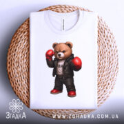 Футболка боксерський ведмідь, біла, складена на плетеній кошику, фон світло-сірий, принт ведмедя в боксерських рукавичках та шкіряному жакеті, з червоними черевиками.