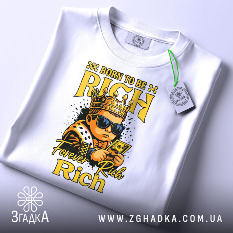 Футболка born to rich, білого кольору, зображена зверху, на ній підвішений ярлик, фон світло-сірий, принт з малюнком хлопчика в короні, в темних окулярах, що тримає гроші, з написами 'BORN TO BE RICH' та 'Forever Rich Rich' у жовтому кольорі.