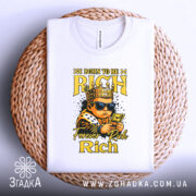 Футболка born to rich, білого кольору, зображена зверху на плетеному кошику, фон білий, принт з малюнком хлопчика в короні, в темних окулярах, що тримає гроші, з написами 'BORN TO BE RICH' та 'Forever Rich Rich' у жовтому кольорі.