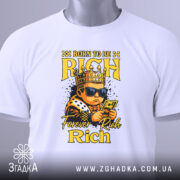 Футболка born to rich, білого кольору, зображена зверху, на ній підвішений ярлик, фон світло-сірий, принт з малюнком хлопчика в короні, в темних окулярах, що тримає гроші, з написами 'BORN TO BE RICH' та 'Forever Rich Rich' у жовтому кольорі.