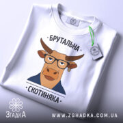 Футболка брутальна скотиняка, білого кольору, зображена зверху на плоскій поверхні, фон світлий, принт з ілюстрацією корови в окулярах та піджаку, прикріплена етикетка з зеленим шнурком.