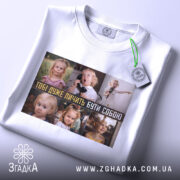 Футболка будь собою завжди. Біла футболка, складена на поверхні, з принтом, що показує дітей у різних ситуаціях. На футболці є етикетка з зеленим шнурком. Фон світлий, акцент на принті та етикетці.