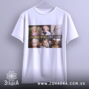 Футболка будь собою завжди. Біла футболка, підвішена на вішалці, з принтом, що містить зображення дітей з різними емоціями. Фон світлий, акцент на принті та формі футболки.