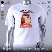 Футболка бути абʼюзером білого кольору, зображена з фронтального ракурсу на манекені, фон однотонний сірий, принт з карикатурним птахом з виразом обличчя, що демонструє впевненість, текст чорного кольору зверху і оранжевого знизу.