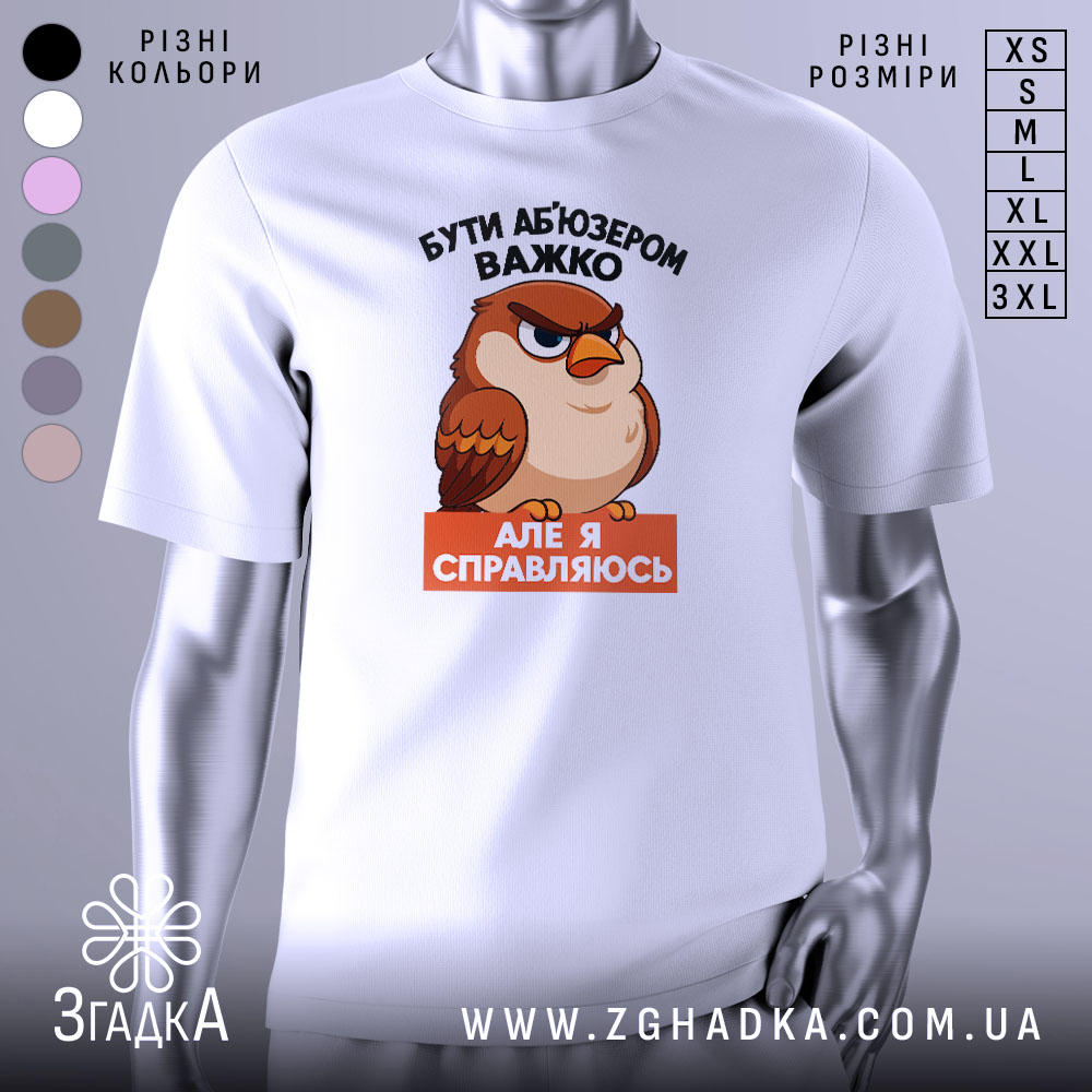 Футболка бути абʼюзером білого кольору, зображена з фронтального ракурсу на манекені, фон однотонний сірий, принт з карикатурним птахом з виразом обличчя, що демонструє впевненість, текст чорного кольору зверху і оранжевого знизу.