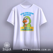 Футболка бути токсіком, біла, зображена на манекені з лівого боку, фон світло-сірий, принт з персонажем у зеленому капюшоні та текстом жовтого кольору.