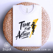 Футболка час для дії, біла, складена на плетеній кошику, фон світлий, принт чорного кольору з жовтою блискавкою та силуетом жінки, що біжить.