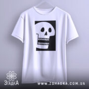 Футболка череп білого кольору, підвішена на вішалці, фон світло-сірий, принт чорного кольору з малюнком черепа, що має великі очі та зуби.