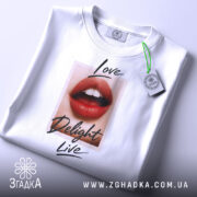 Футболка червоні губи, біла, складена на поверхні, фон світло-сірий, принт з червоними губами та написами 'Love', 'Delight', 'Live', з етикеткою на шнурку.