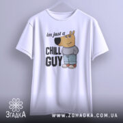 Футболка chill guy стиль, біла, зображена з фронтального ракурсу, підвішена на вішалці, фон світло-сірий, принт з мультяшним ведмедем у джинсах та светрі, текст 'im just a CHILL GUY'.