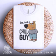 Футболка chill guy стиль, біла, зображена зверху, складена на плетеній кошику, фон білий, принт з мультяшним ведмедем у джинсах та светрі, текст 'im just a CHILL GUY'.