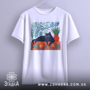 Футболка Чорний кіт спокою білого кольору, підвішена на вішалці, фон світло-сірий. Принт з чорним котом, що лежить на червоній підставці, оточений зеленими рослинами та квітами.