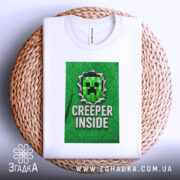 Футболка creeper inside, біла, складена на плетеній кошику, фон світлий, принт з зеленим крипером та написом 'CREEPER INSIDE', видима етикетка на комірці.