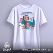 Футболка Далі арт принт, біла, підвішена на вішалці, фон світло-сірий, принт з ілюстрацією Сальвадора Далі, який їсть з миски, з деталями молока, бананів і коробки з написом 'Surreal'.