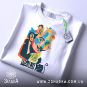 Футболка Далі арт, біла, зображена на столі, фон світло-сірий, принт з обличчям художника, кольорові деталі, текст "I don't do drugs I AM drugs", на комірці етикетка з зеленим шнурком.