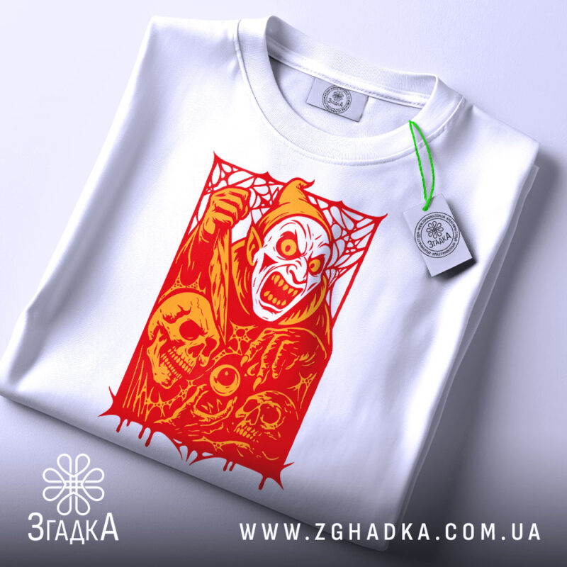 Футболка демон червоний, біла футболка на плоскій поверхні, ракурс зверху, фон світло-блакитний, принт з червоним демоном та черепами, з етикеткою на зеленому шнурку.