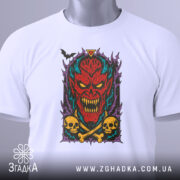 Футболка демонічний яскравий образ, біла, з верхнього ракурсу, на столі, фон світло-сірий, принт з червоним демоном, жовтими черепами та чорними кістками, з зеленим ярличком.