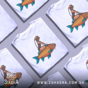 Футболка дівчина на рибі, біла, з фронтального ракурсу, на манекені, з яскравим принтом, де дівчина в аквалангу сидить на великій рибі.