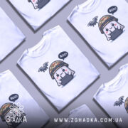 Футболка Дрон під контролем, біла, зображена на манекені, фон світло-сірий, принт з веселим привидом у камуфляжному шоломі, який тримає пульт управління з дроном над головою, текст 'BOO!' у бульбашці.