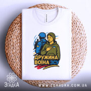 Футболка дружина воїна ЗСУ, біла, складена на плетеній основі, фон білий, принт з жінкою в капюшоні та військовим, кольори принта: жовтий, синій, зелений.