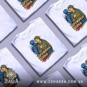 Футболка дружина воїна ЗСУ, біла, зображена на манекені з правого боку, фон світло-сірий, принт з жінкою в капюшоні та військовим, кольори принта: жовтий, синій, зелений.