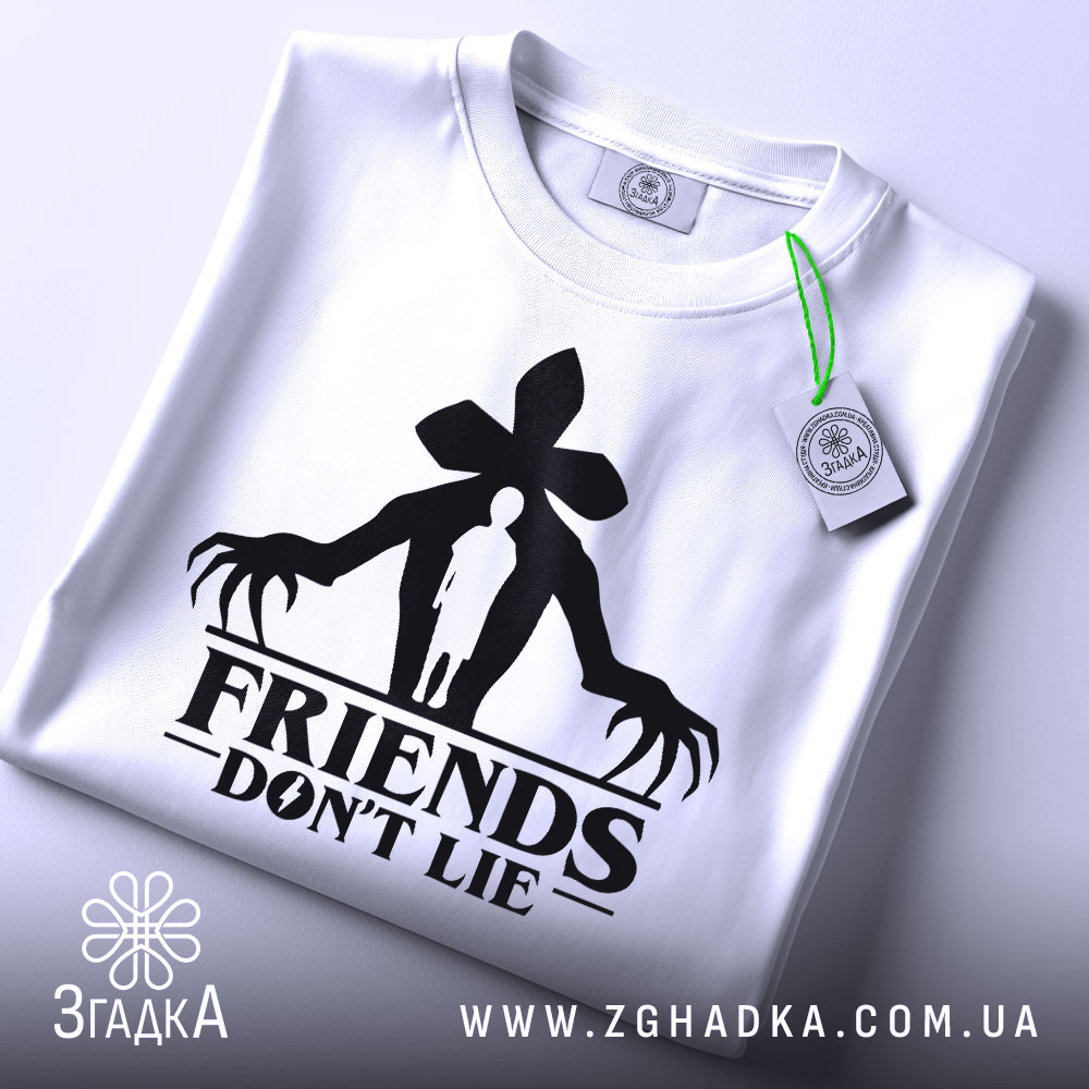 Футболка друзі не брешуть, біла, зображена зверху, складена на поверхні, фон світло-сірий, принт чорного кольору з силуетом людини та великими руками, на футболці є етикетка з зеленим шнурком.