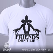 Футболка друзі не брешуть, біла, зображена зверху, складена на поверхні, фон світло-сірий, принт чорного кольору з силуетом людини та великими руками, на футболці є етикетка з зеленим шнурком.