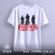 Футболка Друзі не брешуть білого кольору, підвішена на вішалці, фон світло-сірий, принт з трьома фігурами дітей на велосипедах у чорному кольорі, текст 'FRIENDS DON'T LIE' червоного кольору під принтом.