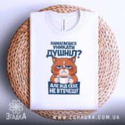 Футболка душніла білого кольору, зображена зверху на плетеній кошику, фон світло-сірий, принт з котом, що тримає чашку, текст на принті синього кольору, видно етикетку на горловині.