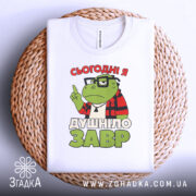 Футболка душнілозавр білого кольору, складена на плетеній основі, фон білий, принт з зеленим персонажем у червоній клітинці та написом 'СЬОГОДНІ Я ДУШНІЛО ЗАВР'.