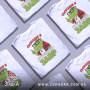 Футболка душнілозавр білого кольору, зображена на манекені з правого боку, фон світло-сірий, принт з зеленим персонажем у червоній клітинці та написом 'СЬОГОДНІ Я ДУШНІЛО ЗАВР'.