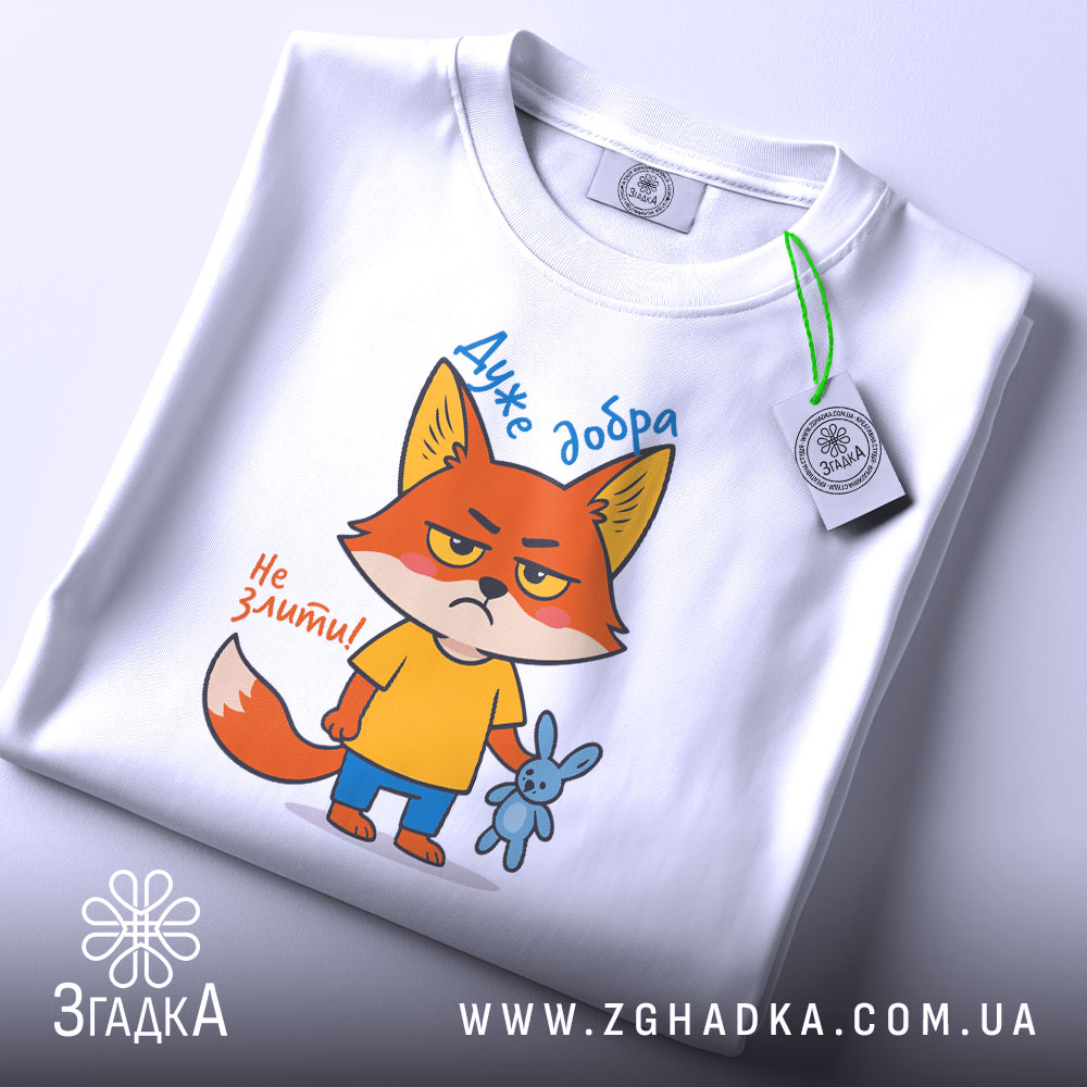 Футболка Дуже добра, білого кольору, зображена зверху, на ній видно принт з мультяшним лисом, який тримає синю іграшку-кролика, текст "Дуже добра" та "Не зліть!", на комірці видно етикетку, фон світло-сірий.
