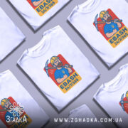 Футболка EBASH білого кольору, зображена з фронтального ракурсу на манекені, фон світло-сірий, принт з чоловіком у жовтій касці з киркою, на синій футболці, з написом 'EBASH 24/7/365'.