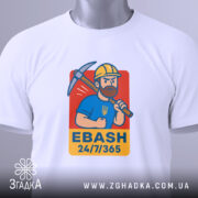 Футболка EBASH білого кольору, зображена зверху, на ній видно принт з чоловіком у жовтій касці з киркою, на синій футболці, з написом 'EBASH 24/7/365', на футболці є етикетка з зеленим шнурком.
