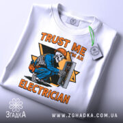 Футболка електрик білого кольору, зображена з верхнього ракурсу, на ній прикріплена етикетка, фон світло-сірий, принт з малюнком скелета-електрика в синій робочій формі, що працює з електричним щитом, текст на принті яскраво-оранжевий.