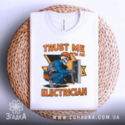 Футболка електрик білого кольору, зображена на плоскому фоні, на плетеній кошику, фон світло-сірий, принт з малюнком скелета-електрика в синій робочій формі, що працює з електричним щитом, текст на принті яскраво-оранжевий.