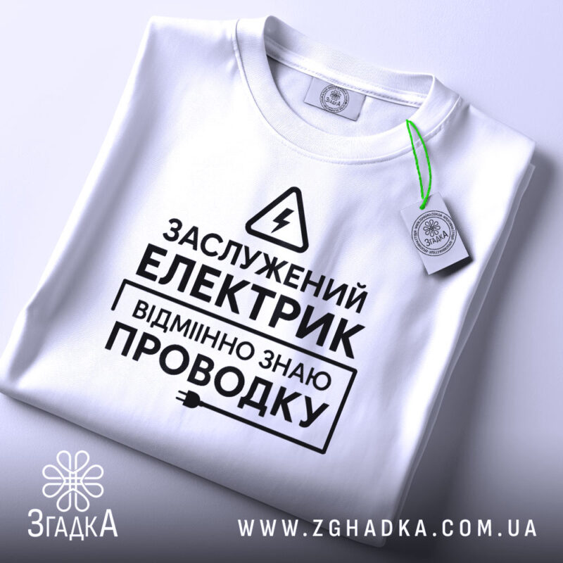 Футболка електрик заслужений, біла, складена на поверхні, фон світло-сірий, принт чорного кольору з текстом та символом блискавки, на комірці є етикетка.