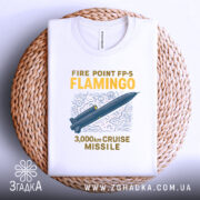 Футболка фламіго білого кольору, складена на плетеній кошику, ракурс зверху, фон білий, принт з малюнком ракети та текстом "FIRE POINT FP-5 FLAMINGO 3,000km CRUISE MISSILE" у жовтому та синьому кольорах.